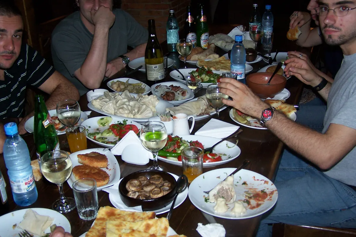Guests seated around a dark wooden table crowded with plates of Georgian dishes, bread, wine glasses and bottles